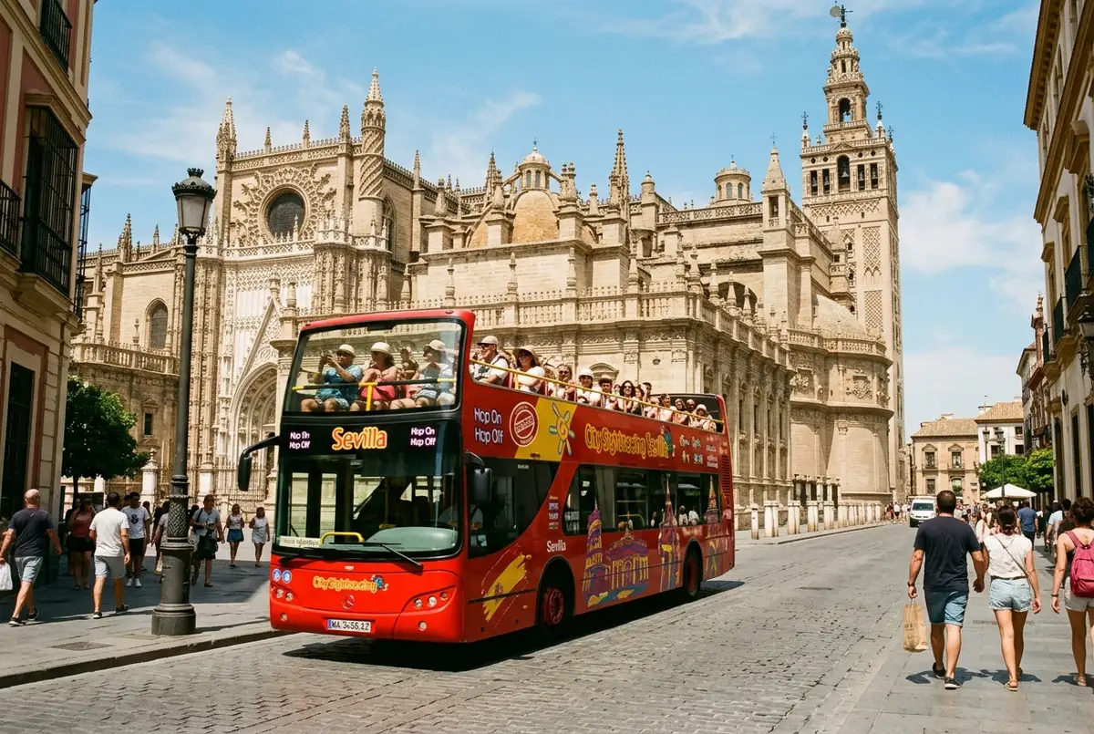 Autobus turistico descapotable de City Sightseeing pasando junto a la Catedral de Sevilla con turistas en la planta superior, sol de mediodia, escena city sightseeing sevilla paseo en barco