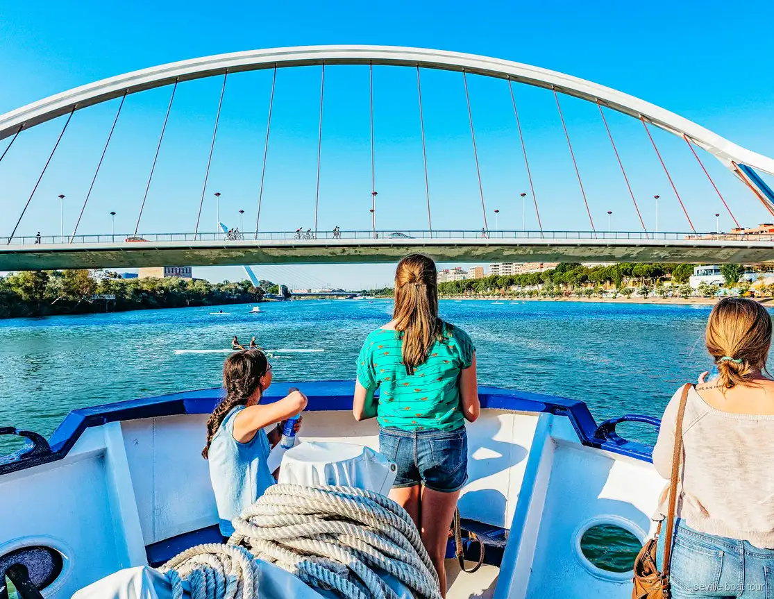 Passeggeri a prua durante un giro in barca a Siviglia verso l'arco bianco del ponte della Barqueta