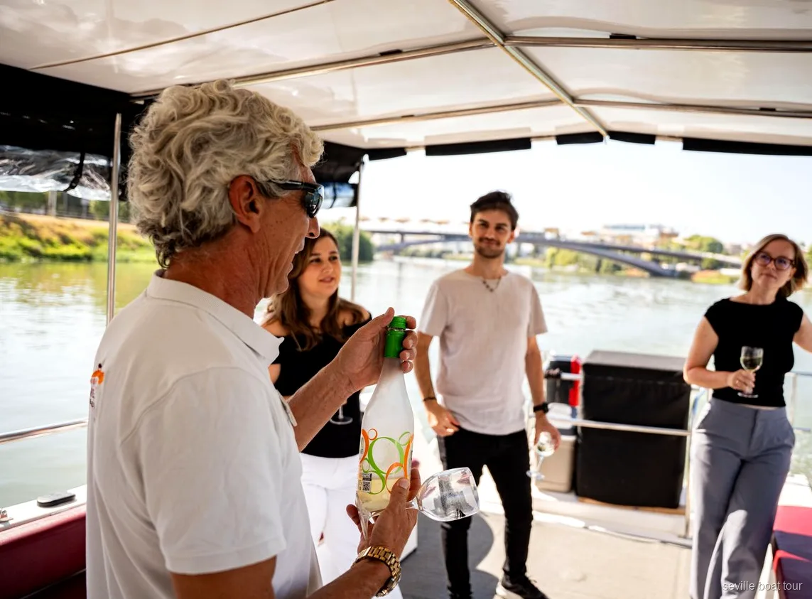 Anfitrión sirviendo vino a los pasajeros bajo el toldo de un paseo en barco por Sevilla