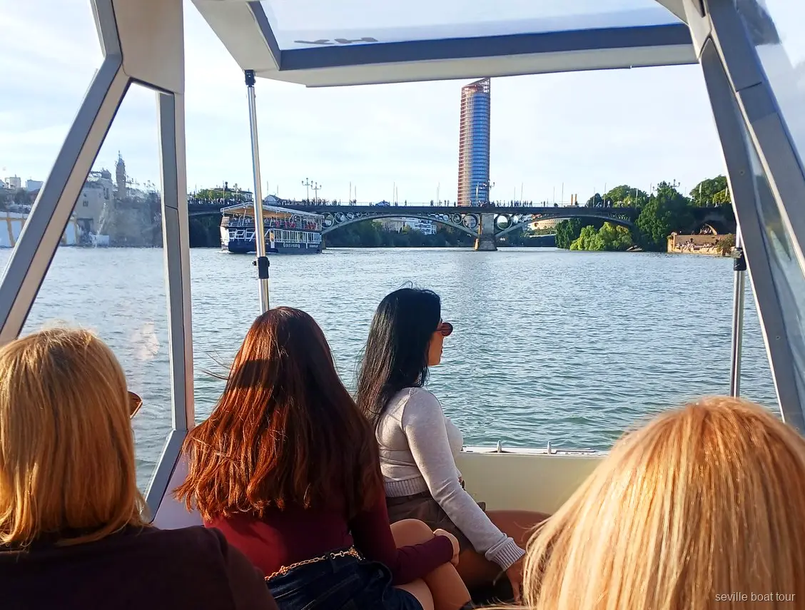 Passeggere sotto la tettoia di un giro in barca privato a Siviglia verso il ponte di Triana e Torre Sevilla
