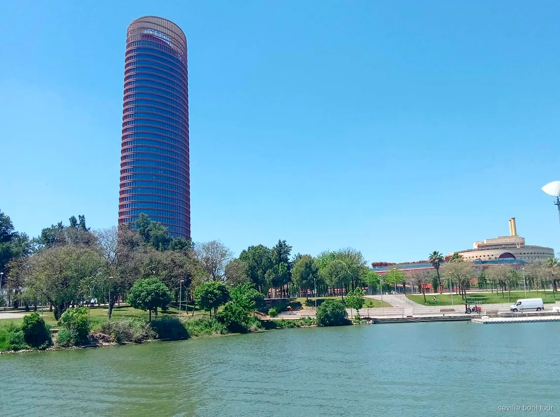 Torre Sevilla y la orilla verde de la Cartuja desde un paseo en barco por Sevilla en el Guadalquivir